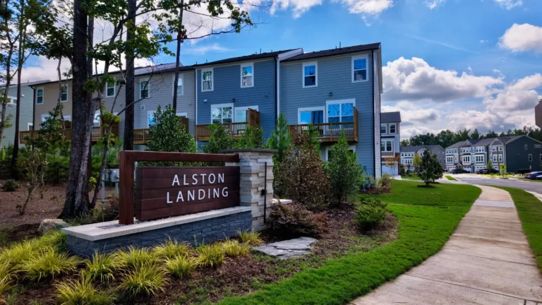 Rows of three-story townhomes behind the Alston Landing sign, with a sidewalk curving past new landscaping