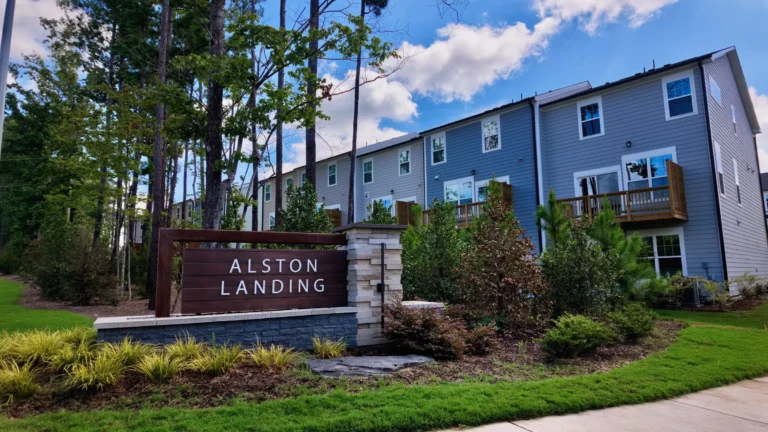Alston Landing stone and wood entrance sign in front of three-story blue-gray townhomes with balconies