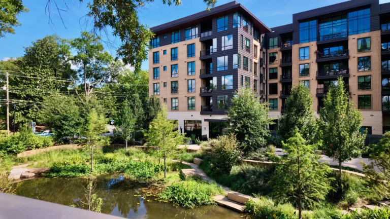 Six-story apartment building of brick and dark panels overlooking a planted pond and gardens