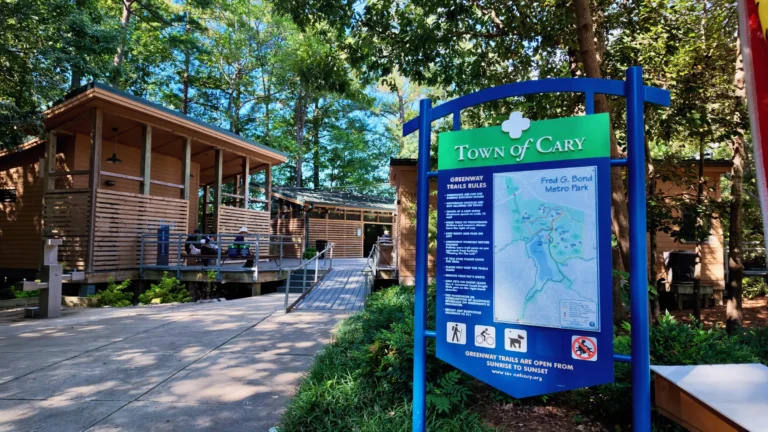Town of Cary greenway trail sign with rules and a Fred G. Bond Metro Park map, the boathouse behind