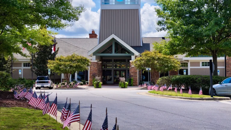 Entrance of the Bradford Hall clubhouse with a tall tower, small American flags lining the curb and cars parked out front