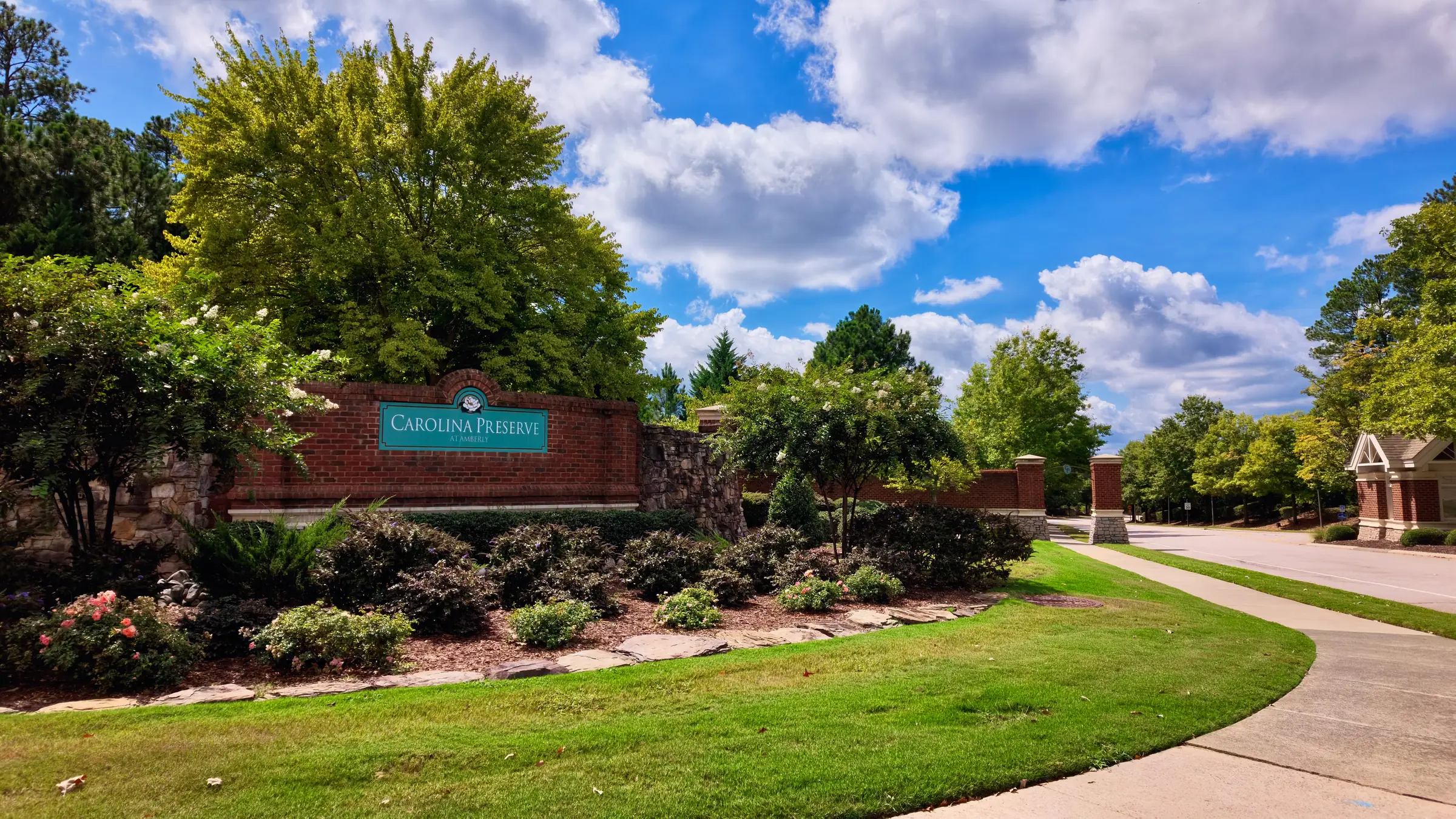 Carolina Preserve brick entrance wall set behind a wide lawn and landscaped beds, with brick gate pillars down the road