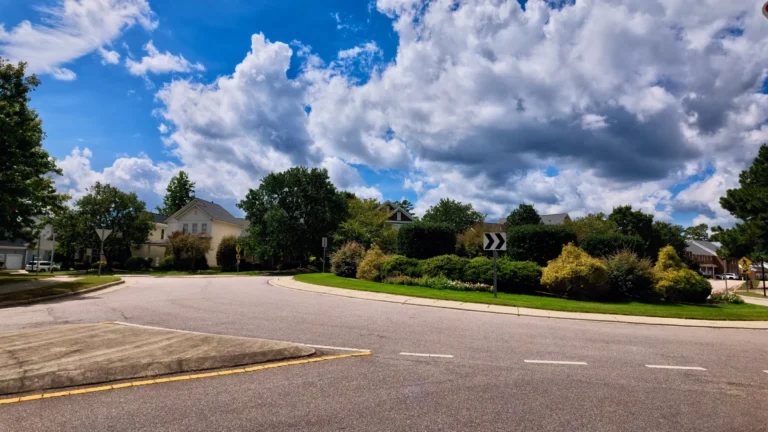 Curving neighborhood road with a landscaped median island and homes set back behind trees