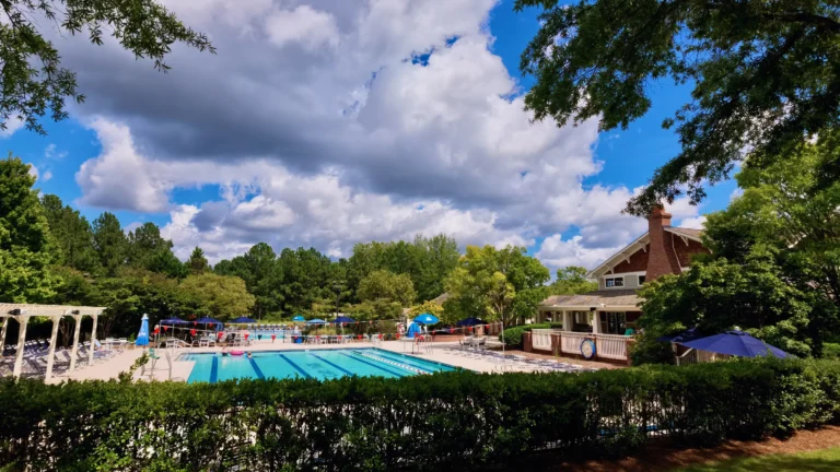 Outdoor pool deck with a white pergola, lounge chairs and a pool house under a cloudy blue sky