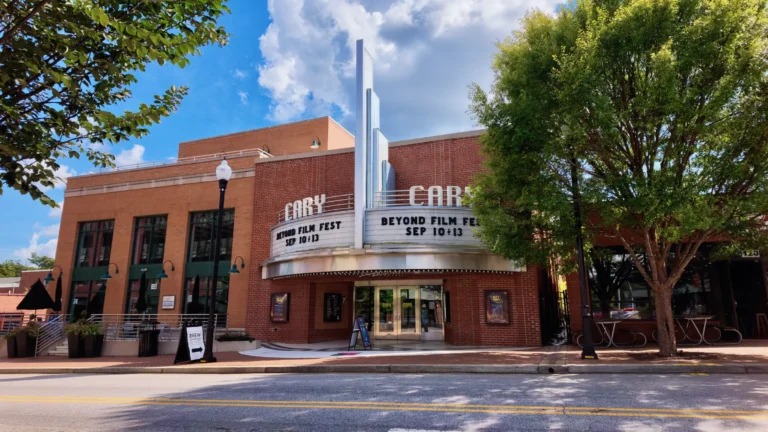 Brick facade of The Cary Theater with its vertical art deco sign and marquee, framed by street trees