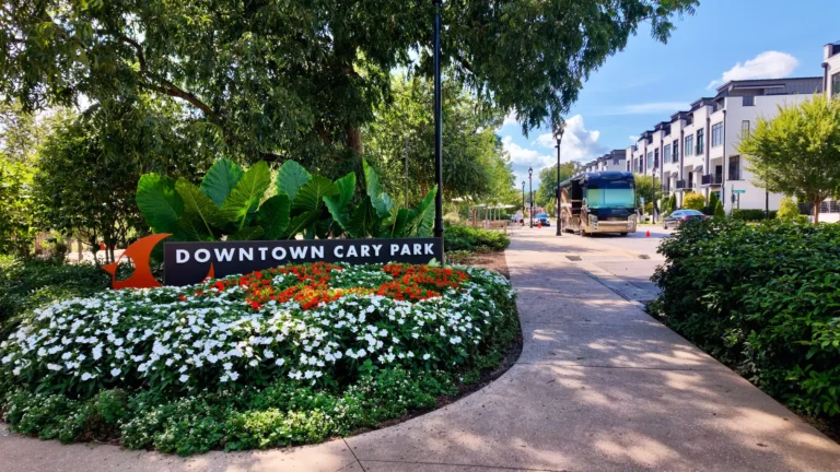 Downtown Cary Park sign in a round bed of white and orange flowers beside a paved path