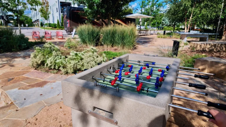 Concrete outdoor foosball table on flagstone paving surrounded by ornamental grasses