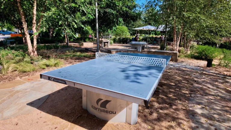 Blue concrete ping pong table on a sandy patch under trees