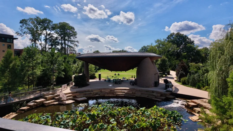 Pond filled with lily pads and stepping stones in front of an open-air stage under a curved roof