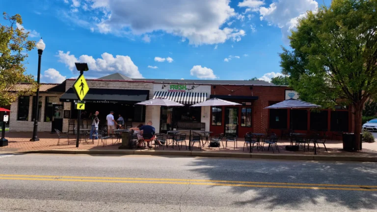 Brick storefronts with striped awnings and a patio of umbrella tables along a downtown street