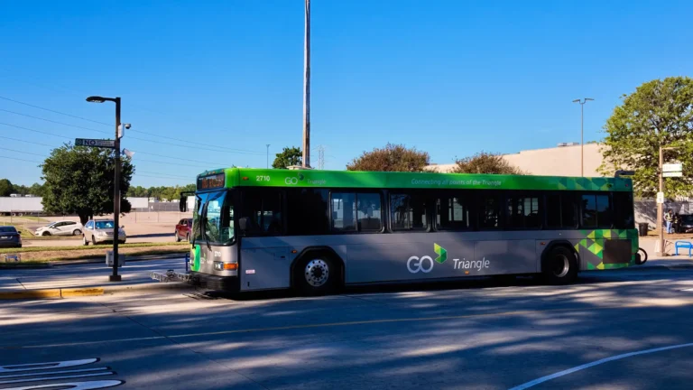 Green and gray GoTriangle bus pulling through the Regional Transit Center under a clear sky
