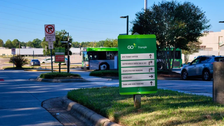 Green GoTriangle sign pointing to the RTC ticket office, park and ride parking and Uber and Lyft pickup, with a bus behind it