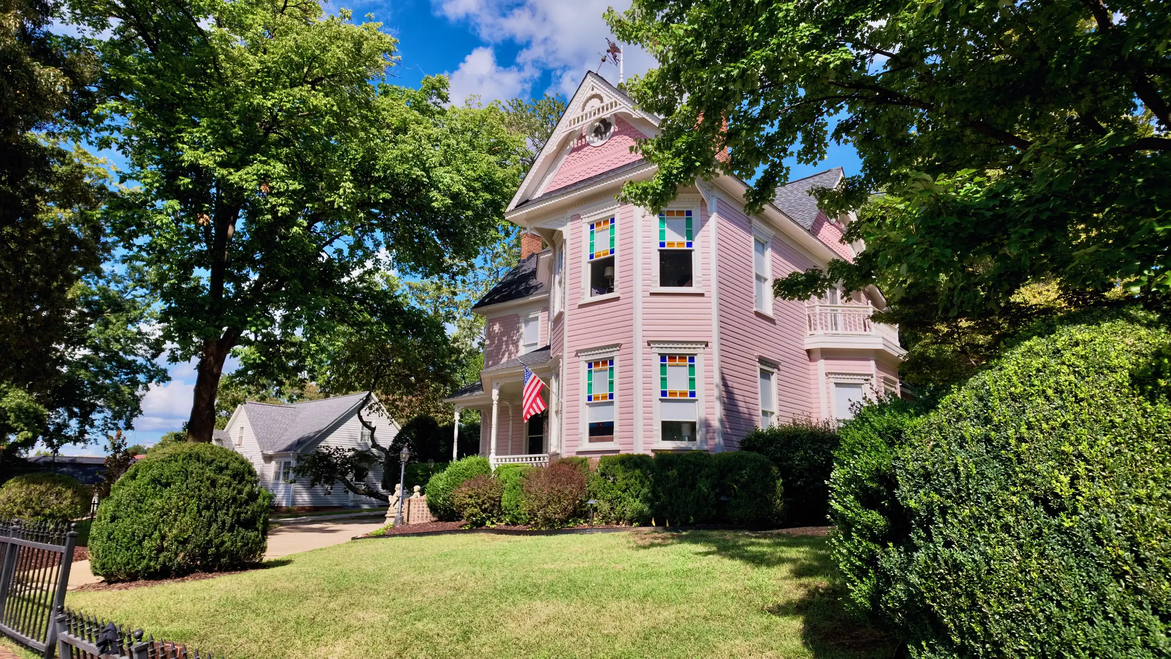 Pink Queen Anne house with a three-story tower and corner turret behind a lawn and trimmed shrubs