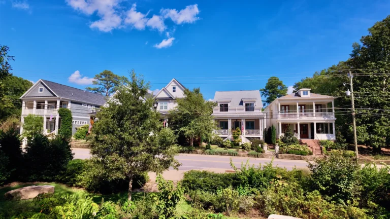 Row of two-story houses with front porches across a street, seen from the park's gardens