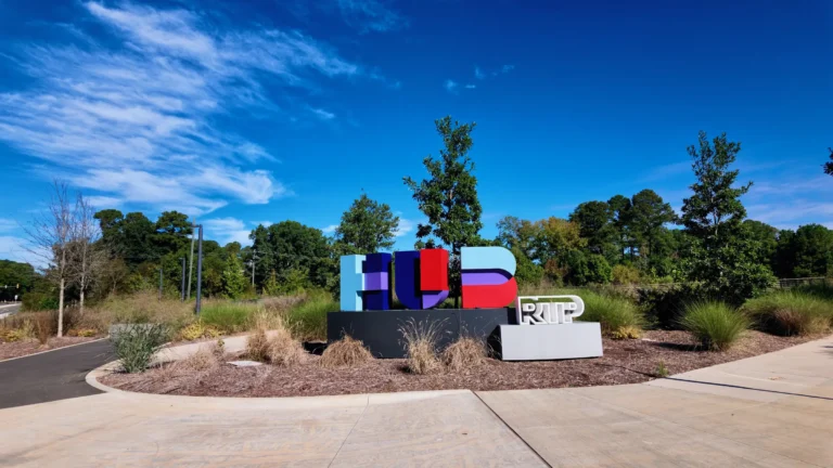 Large colorful Hub RTP letters in a landscaped bed with grasses beside a curving road