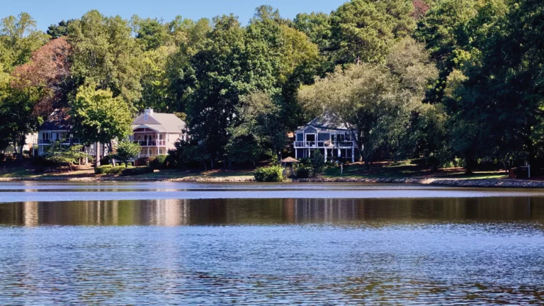 Lakefront homes with decks and screened porches under tall trees, reflected in calm water