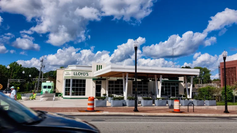 Restored 1950s service station turned restaurant, white with a flat canopy roof and a Lloyd's sign, orange traffic barrels in front