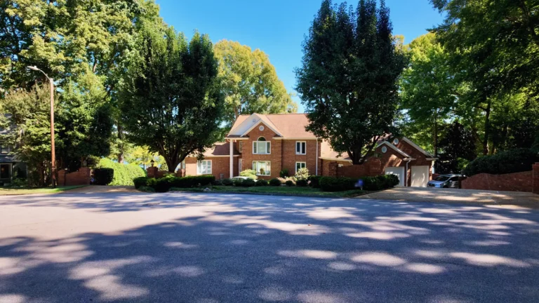 Brick two-story home with a two-car garage at the end of a wide street, trees on both sides