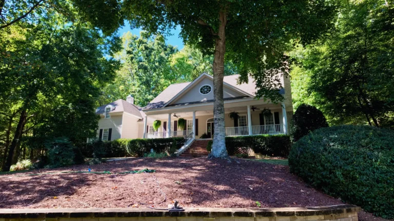 Two-story home with a deep white front porch and a round gable window, under a large shade tree