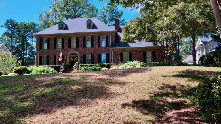 Brick two-story colonial with black shutters and dormers on a rise behind a wide lawn
