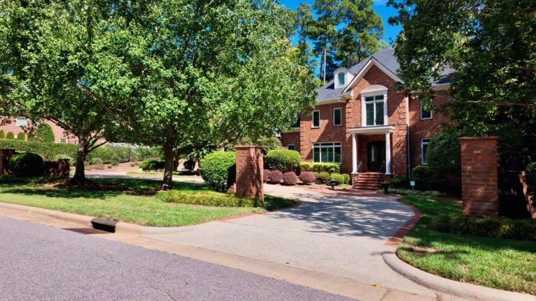 Brick two-story Georgian-style house behind brick driveway pillars and mature trees
