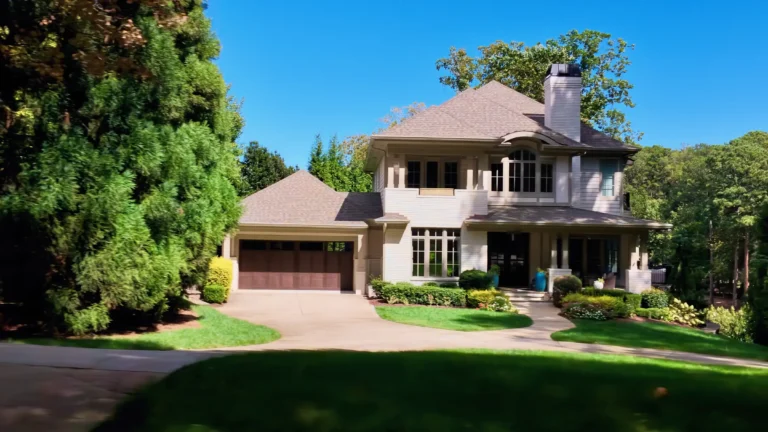 Two-story light stone home with a wood garage door, a covered front porch and landscaped beds