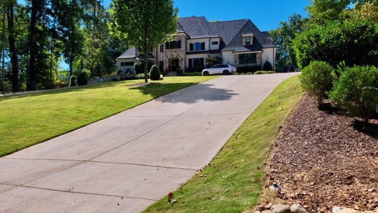 Long concrete driveway climbing a green lawn to a large stone and shingle house on a hill