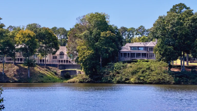 Two large lakefront homes with multi-level decks on a wooded hillside above the water