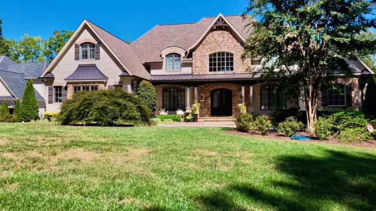 Large stone and brick home with gables, a metal-roofed porch and a wide front lawn