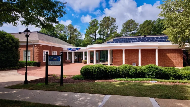 Front walk and lawn of Morrisville Town Hall, a one-story brick building with a curved white colonnade
