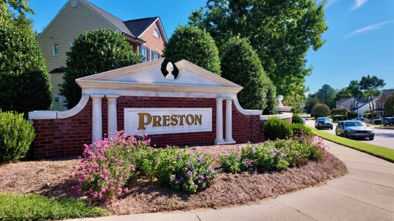 Brick entrance wall with white columns, a pediment and gold Preston lettering behind pink and purple flowers