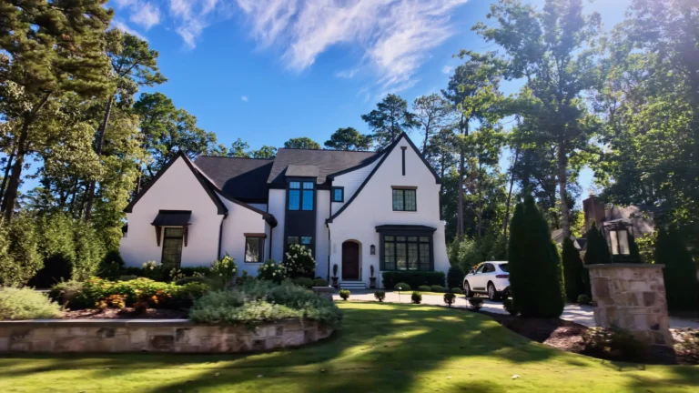 White modern farmhouse-style house with a dark steep roofline and black windows, a stone pillar in the foreground
