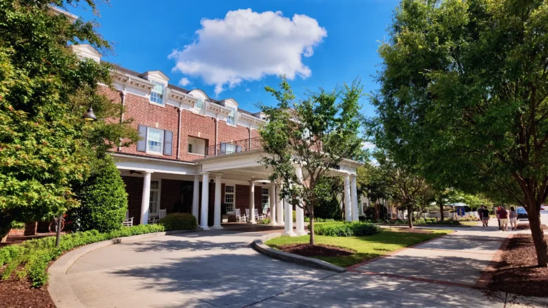 Brick building with a white-columned covered carport over a curved driveway, under a blue sky