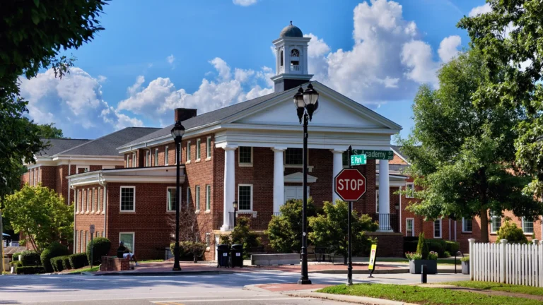 Georgian-style brick building with white columns and a cupola at a street corner with a stop sign and lampposts